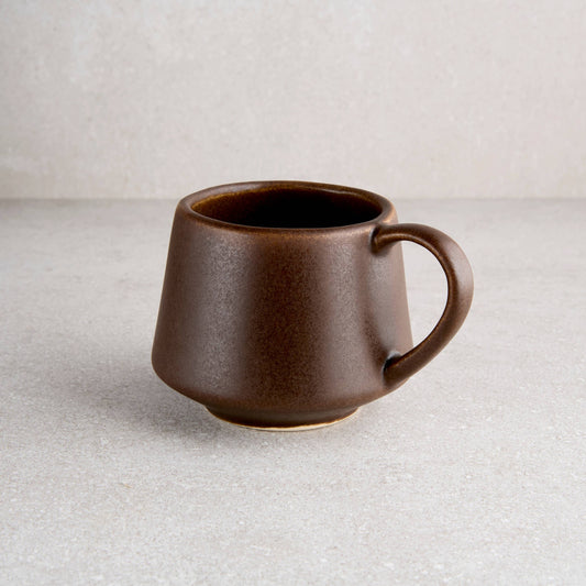 Brown ceramic mug on a light gray surface with a neutral background