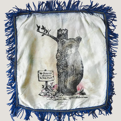 Decorative square with a bear illustration and 'No Hugging Allowed' sign, framed with blue fringe.