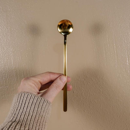 Gold spoon held by a hand against a beige wall